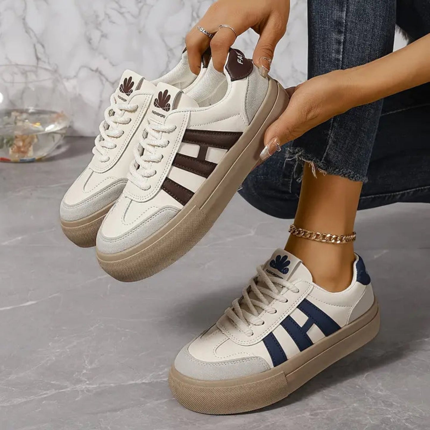White low-top sneakers with blue 3-stripe panels and lace-up closure, tan soles.