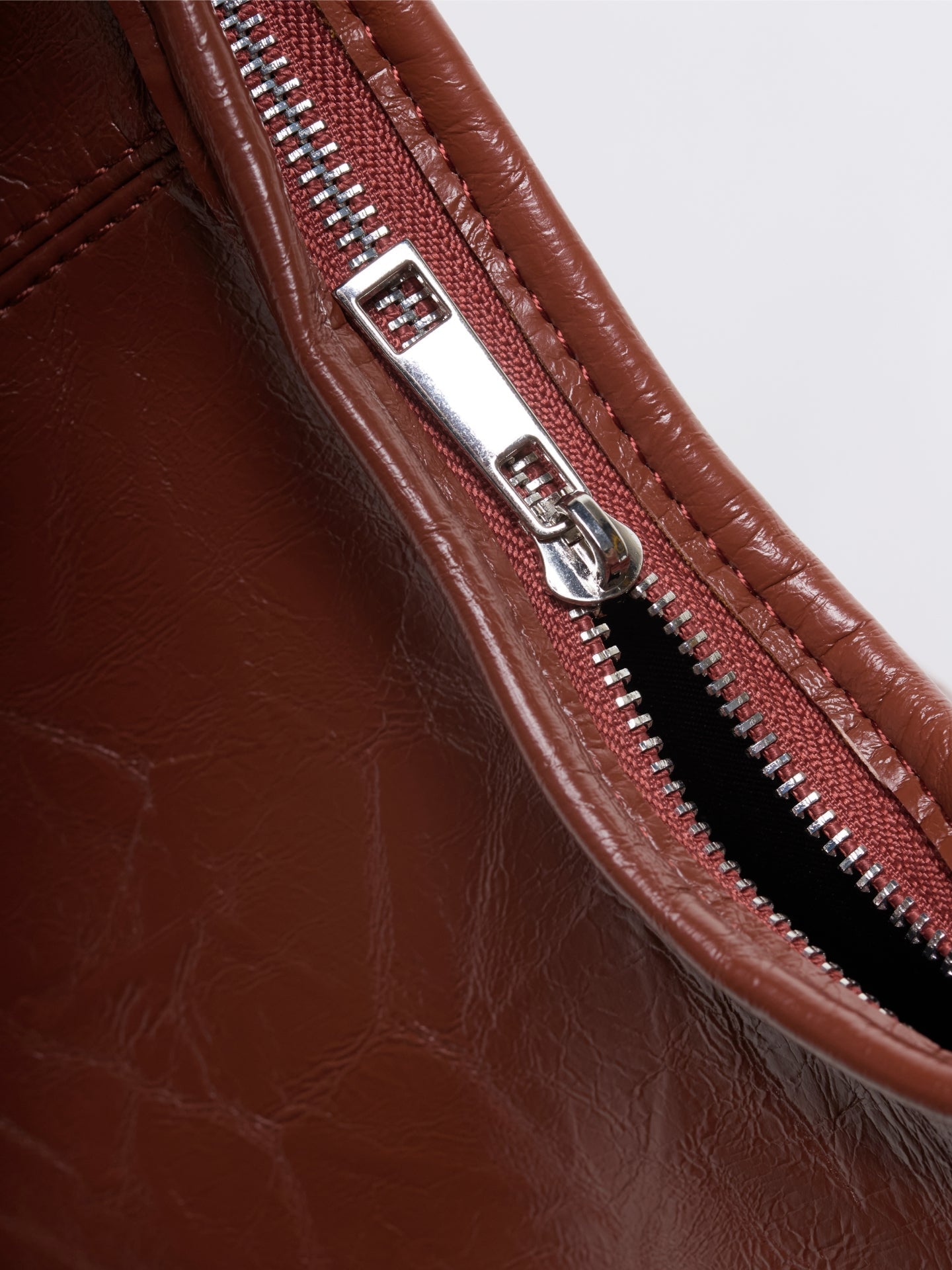 Brown vegan leather tote bag detail: front zipper track with silver hardware.