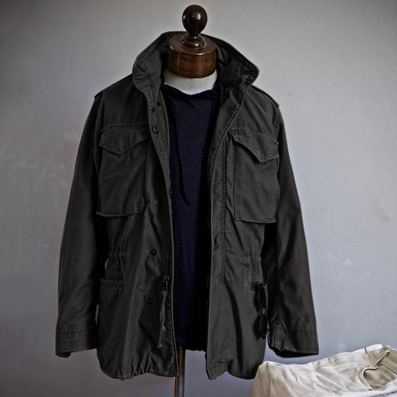 Men's military field jacket, black with buttoned front and flap pockets on mannequin