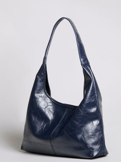 Distressed vegan leather tote bag in dark blue with wide top handles and slouch shape.