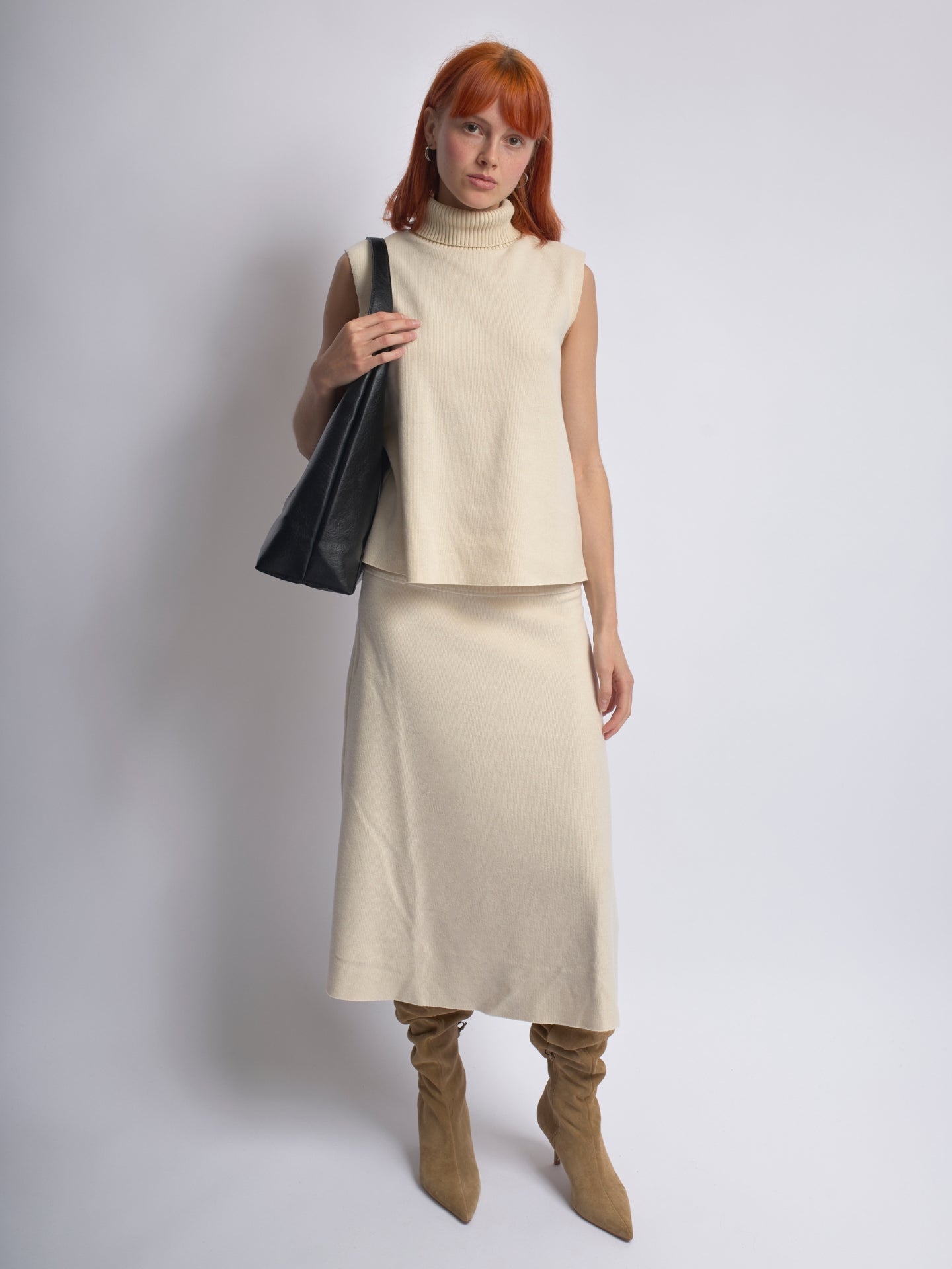 Black leather shoulder bag held over the shoulder by a woman in a light outfit.