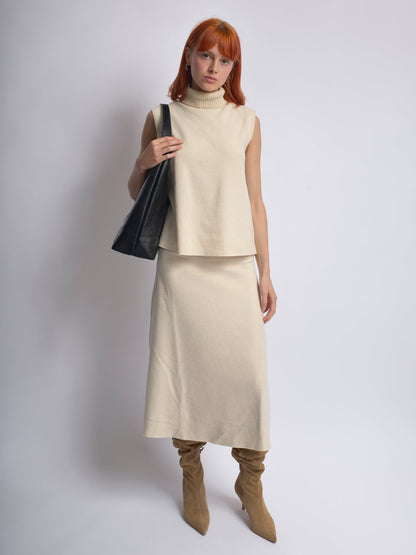 Black leather shoulder bag held over the shoulder by a woman in a light outfit.