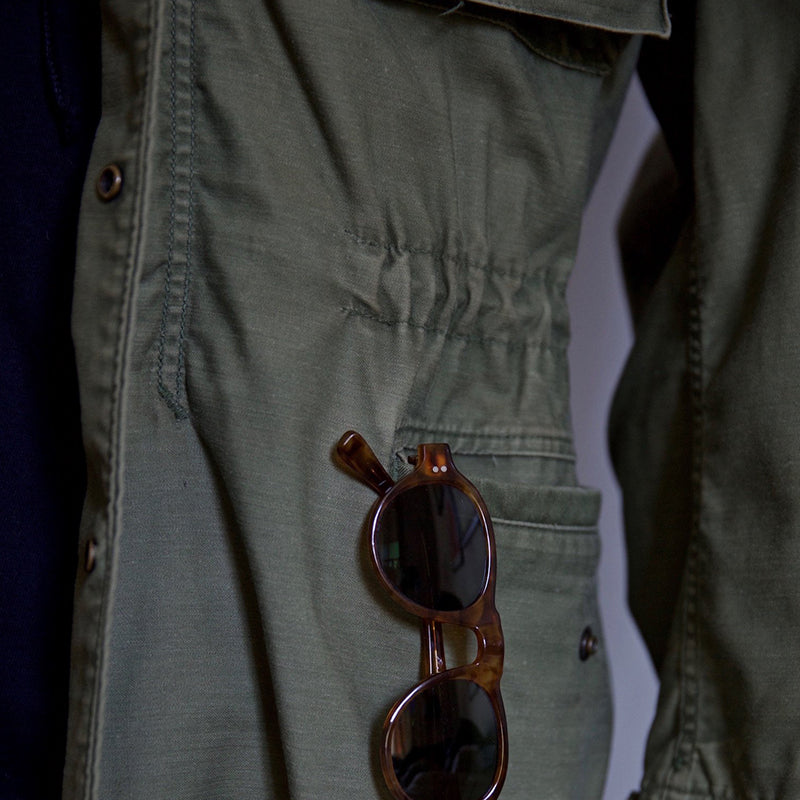 Olive green field jacket close-up: chest pocket, buttons, textured fabric
