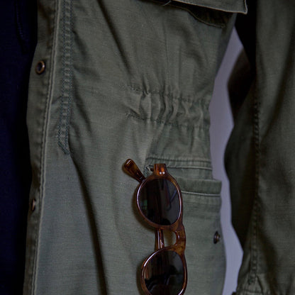 Olive green field jacket close-up: chest pocket, buttons, textured fabric