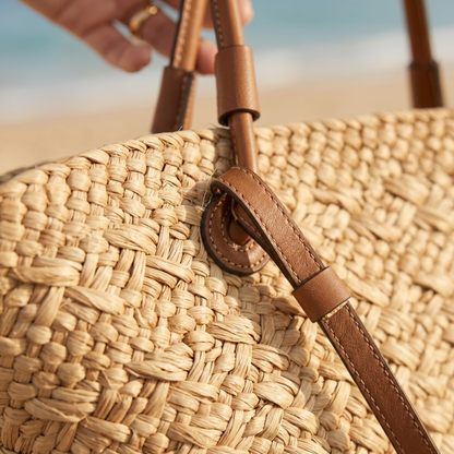 Close-up of woven rattan tote with brown leather loop and stitching detail.
