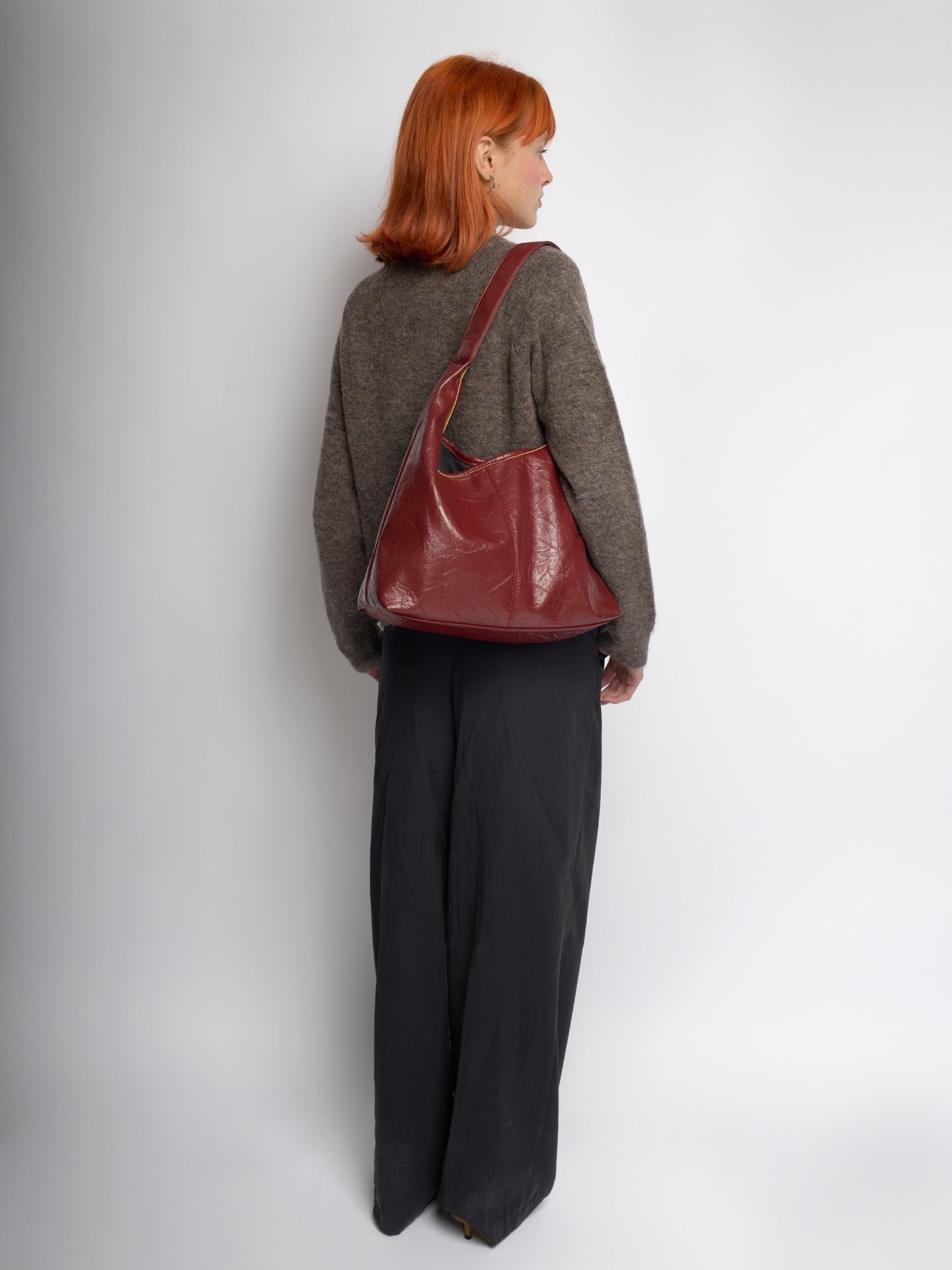 Burgundy distressed vegan leather tote bag worn over shoulder, back view