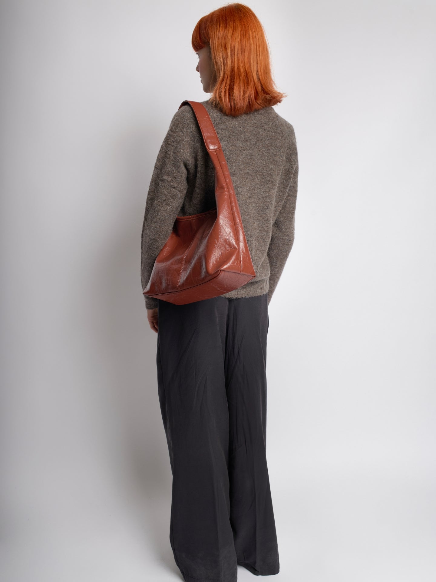 Distressed vegan leather tote bag in brown, carried over the shoulder with front pocket