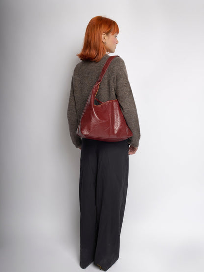 Burgundy distressed vegan leather tote worn over shoulder, side view