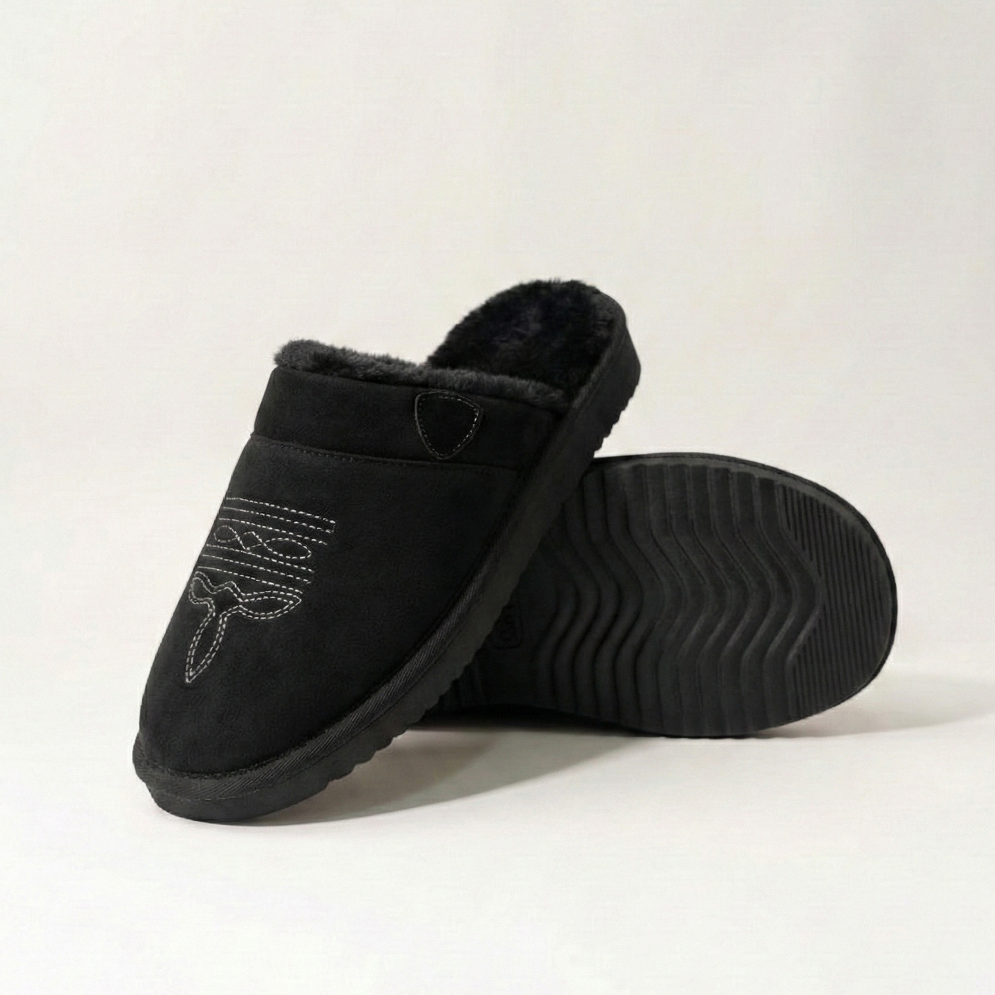 Cowboy slippers in black suede with white patterned embroidery, faux-fur lining, and treaded sole.