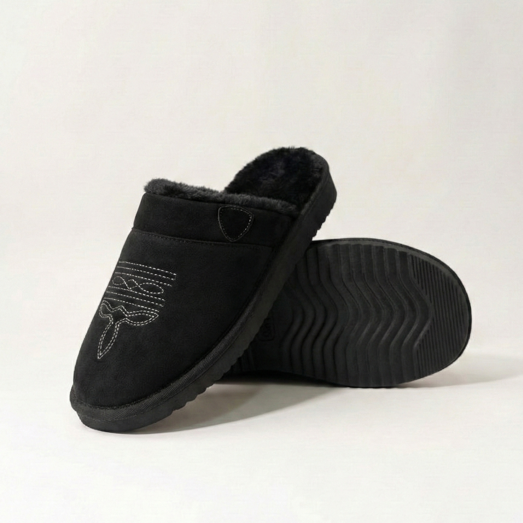Cowboy slippers in black suede with white patterned embroidery, faux-fur lining, and treaded sole.