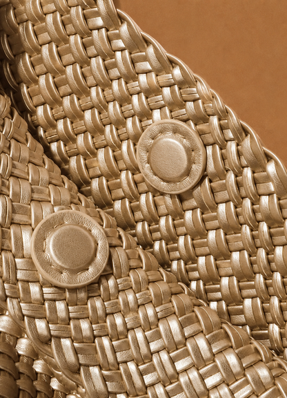 Gold-toned woven tote bag detail with round metallic snap ornament