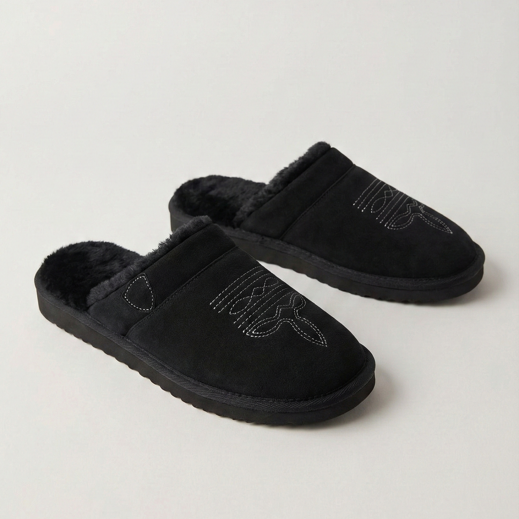 Pair of black slip-on cowboy slippers with faux-fur lining and curved stitch design
