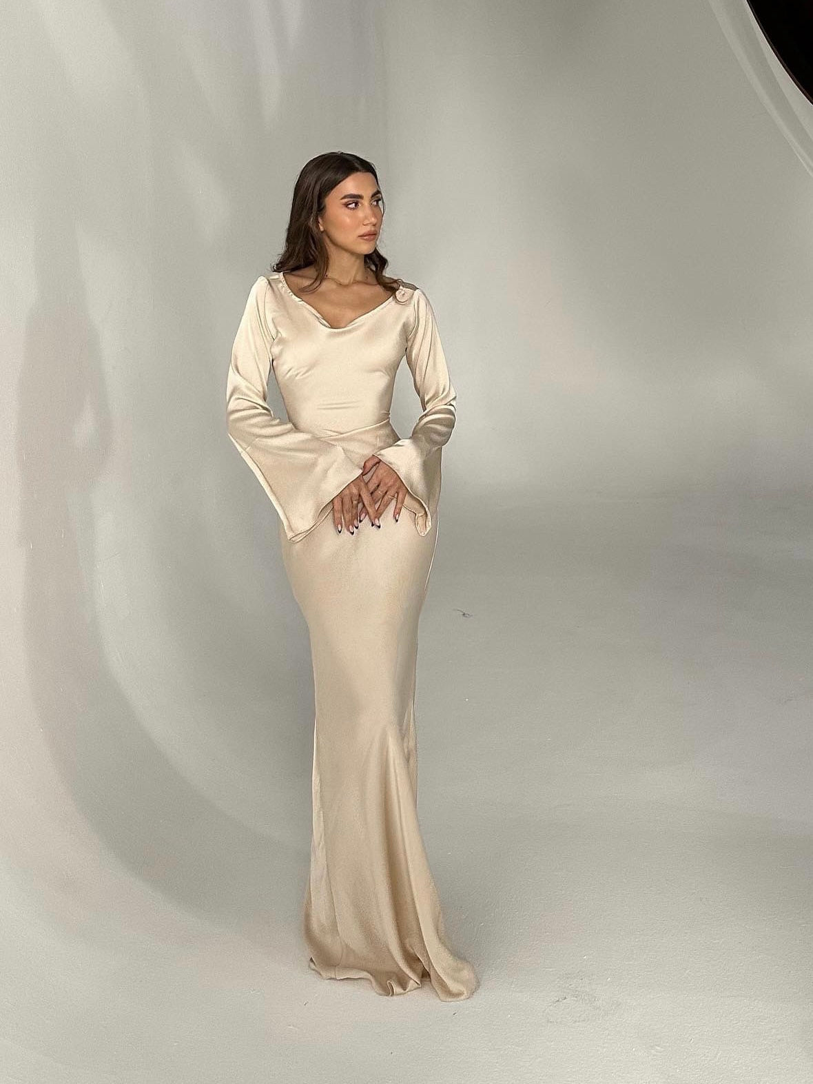 Beige long-sleeve maxi dress with scoop neckline, fitted silhouette, and draped sleeves