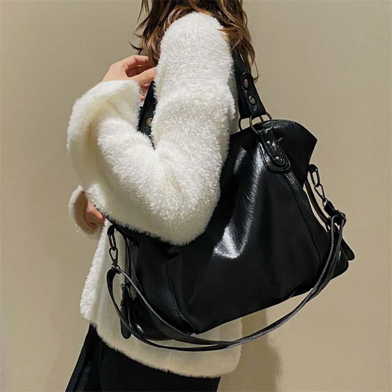 Black vegan leather handbag with top handles, side strap details, and crossbody chain strap
