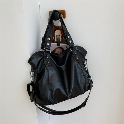 Black vegan leather handbag hanging with two top handles and side zipper detailing