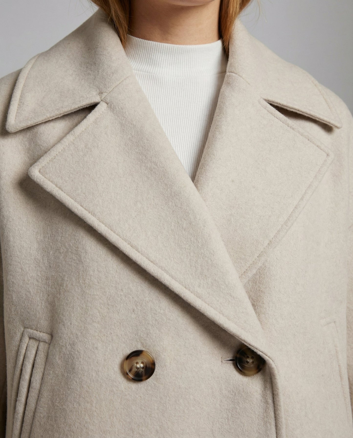 Cropped double-breasted jacket lapel close-up in light beige with gold-tone buttons
