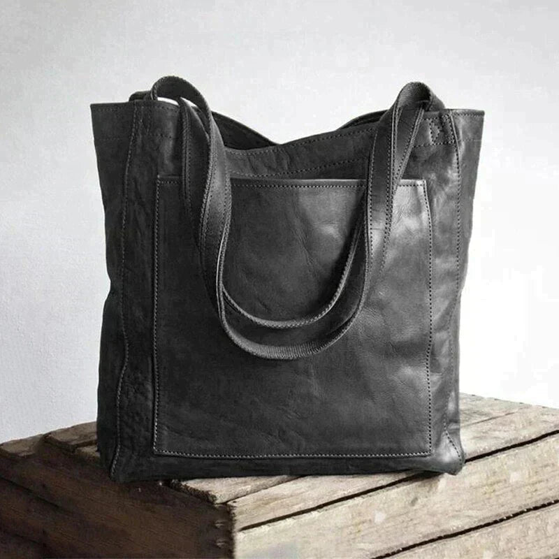 Black leather tote bag with wide handles and stitched front panel