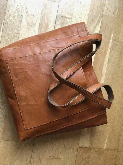 Brown leather tote bag lying flat with stitched seams and crossbody-style straps