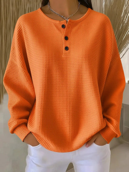 Orange waffle-knit henley jumper with black button placket and long sleeves