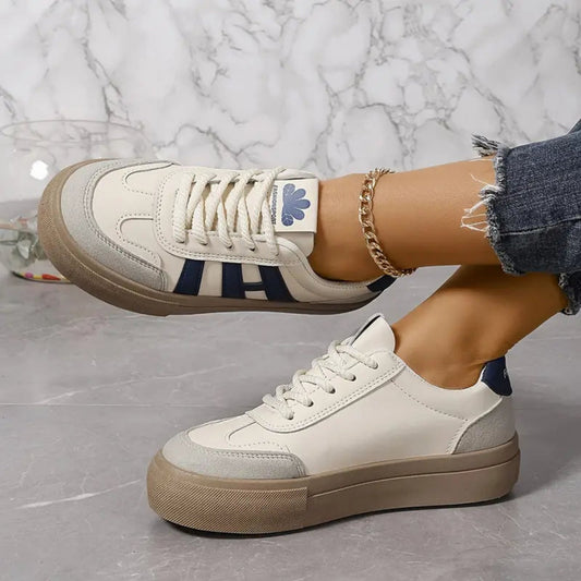 White low-top sneakers with blue 3-stripe sides, lace-up front, tan rubber sole.