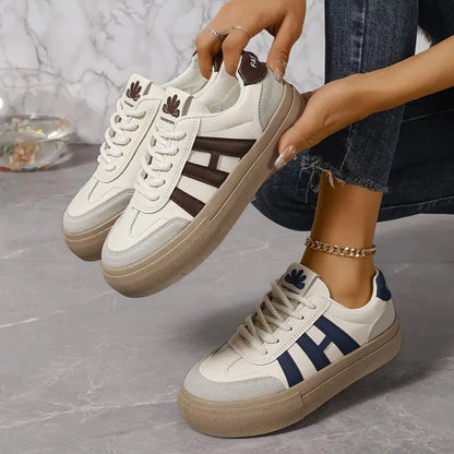 White low-top sneakers with blue 3-stripe panels and lace-up closure, tan soles.