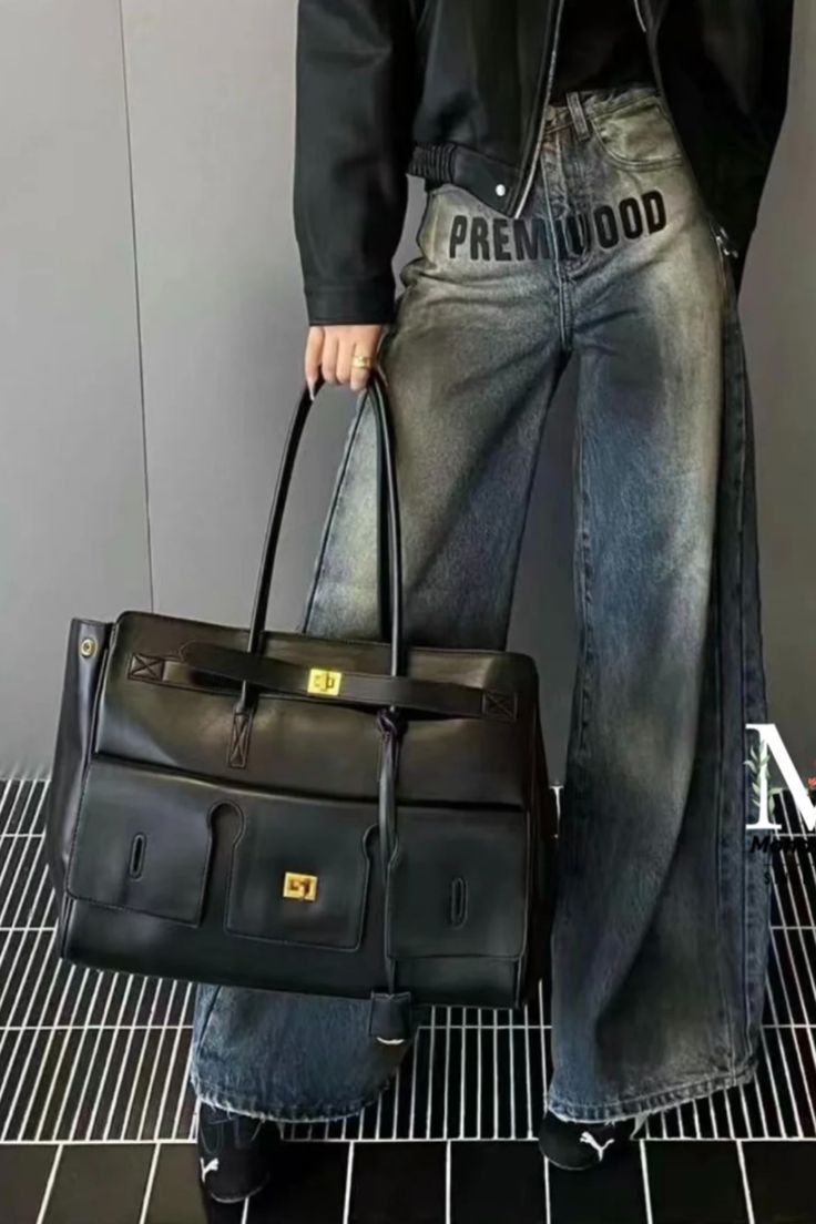Black structured handbag worn with jeans; top handles and front gold-tone hardware