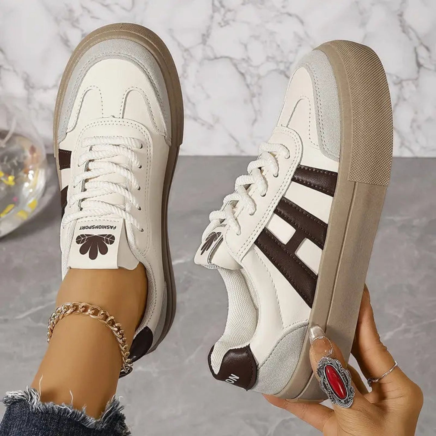 White sneakers with brown 3-stripe detail, lace-up, tan sole, floral tongue patch.